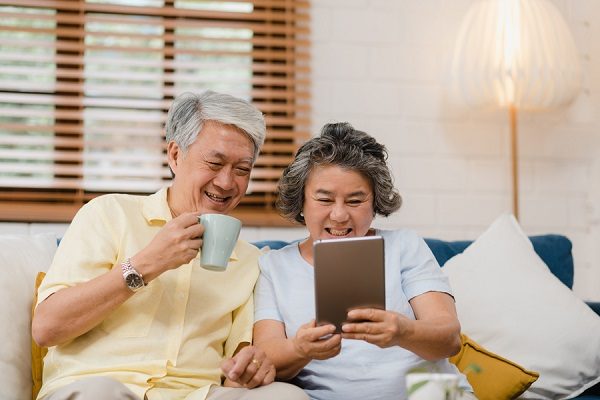 Asian elderly couple using tablet and drinking coffee in living